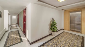 A hotel corridor with patterned floor tiles, a potted plant, and an elevator. - Vina Spa Hotel (Hue)