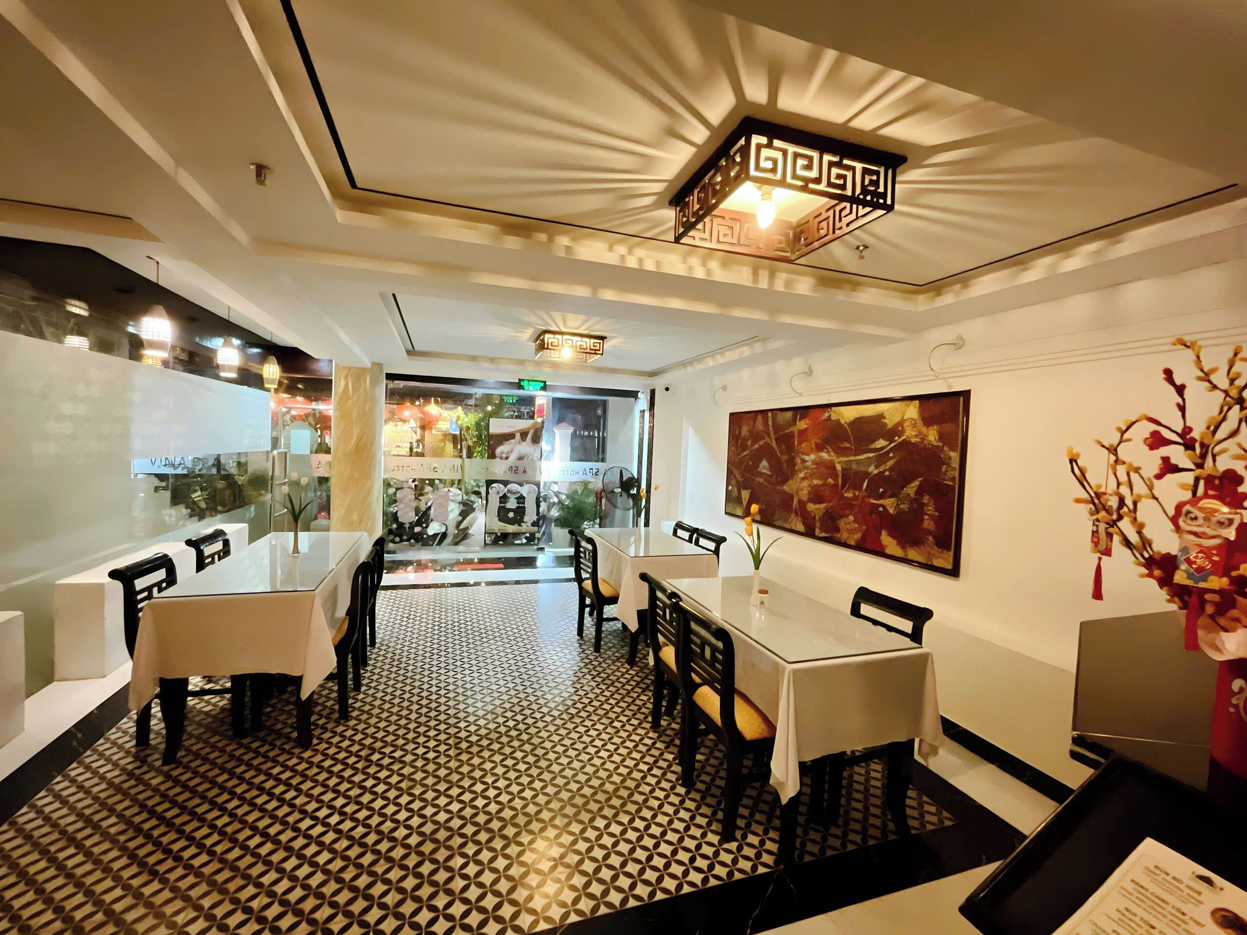 A restaurant interior with a patterned floor, tables with chairs, a ceiling light fixture, and a large abstract painting on the wall.