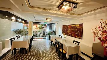 A restaurant interior with a patterned floor, tables with chairs, a ceiling light fixture, and a large abstract painting on the wall.