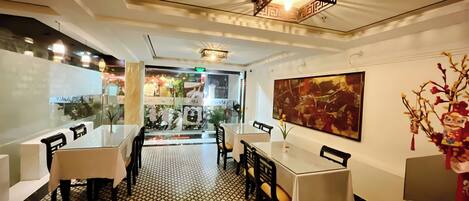 A restaurant interior with a patterned floor, tables with chairs, a ceiling light fixture, and a large abstract painting on the wall.