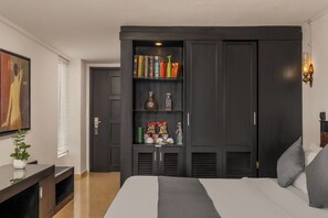 Un dormitorio con una cama grande, un armario con estantes, un cuadro en la pared y una mesita de noche con una planta.