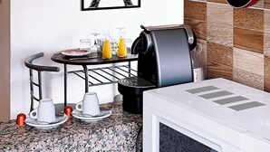 Cozinha com painel de azulejos, máquina de café, chaleira e suporte para panelas suspenso.