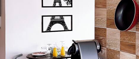 Una cocina con salpicadero de azulejos, máquina de café, hervidor y un colgador para ollas.