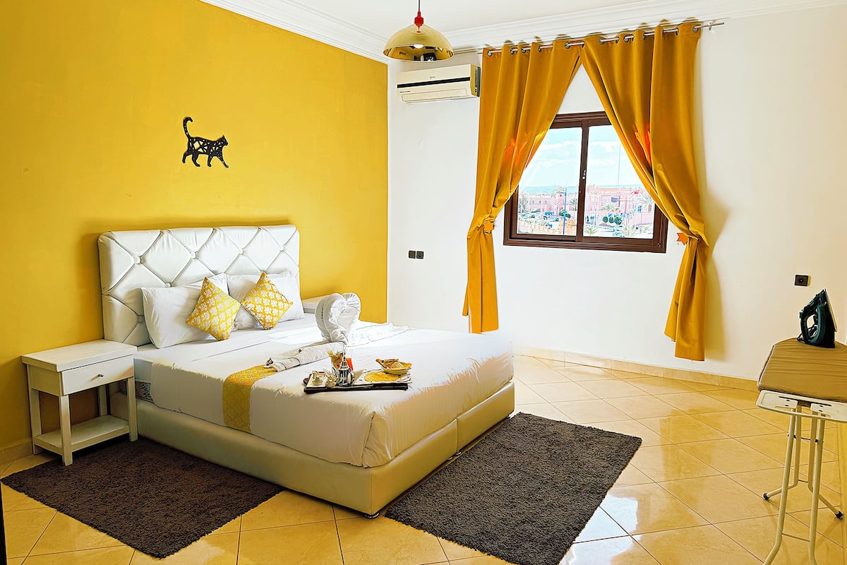 Habitación de hotel con cama, mesita de noche, ventana con cortinas y vistas al exterior.