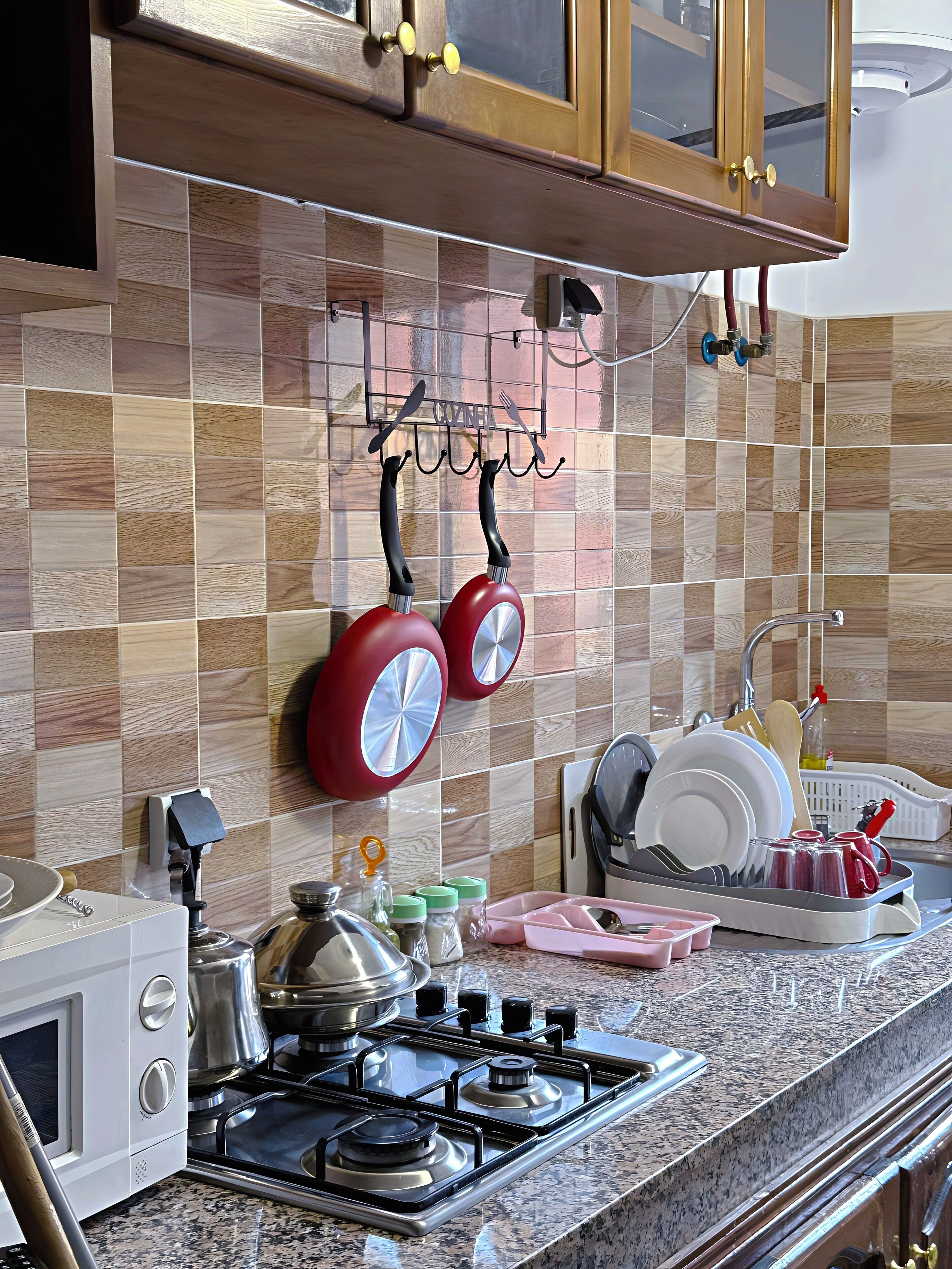 Een keuken met een gasfornuis, een magnetron en een spoelbak. Er hangen pannen en er is een afdruiprek met servies.