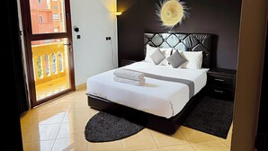 Quarto de hotel com cama, mesa de cabeceira, abajur e vista para a varanda externa.