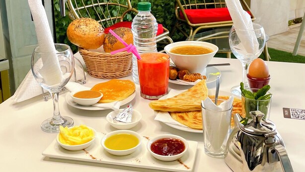 Uma mesa de café da manhã com diversos alimentos, um letreiro de neon e duas cadeiras.