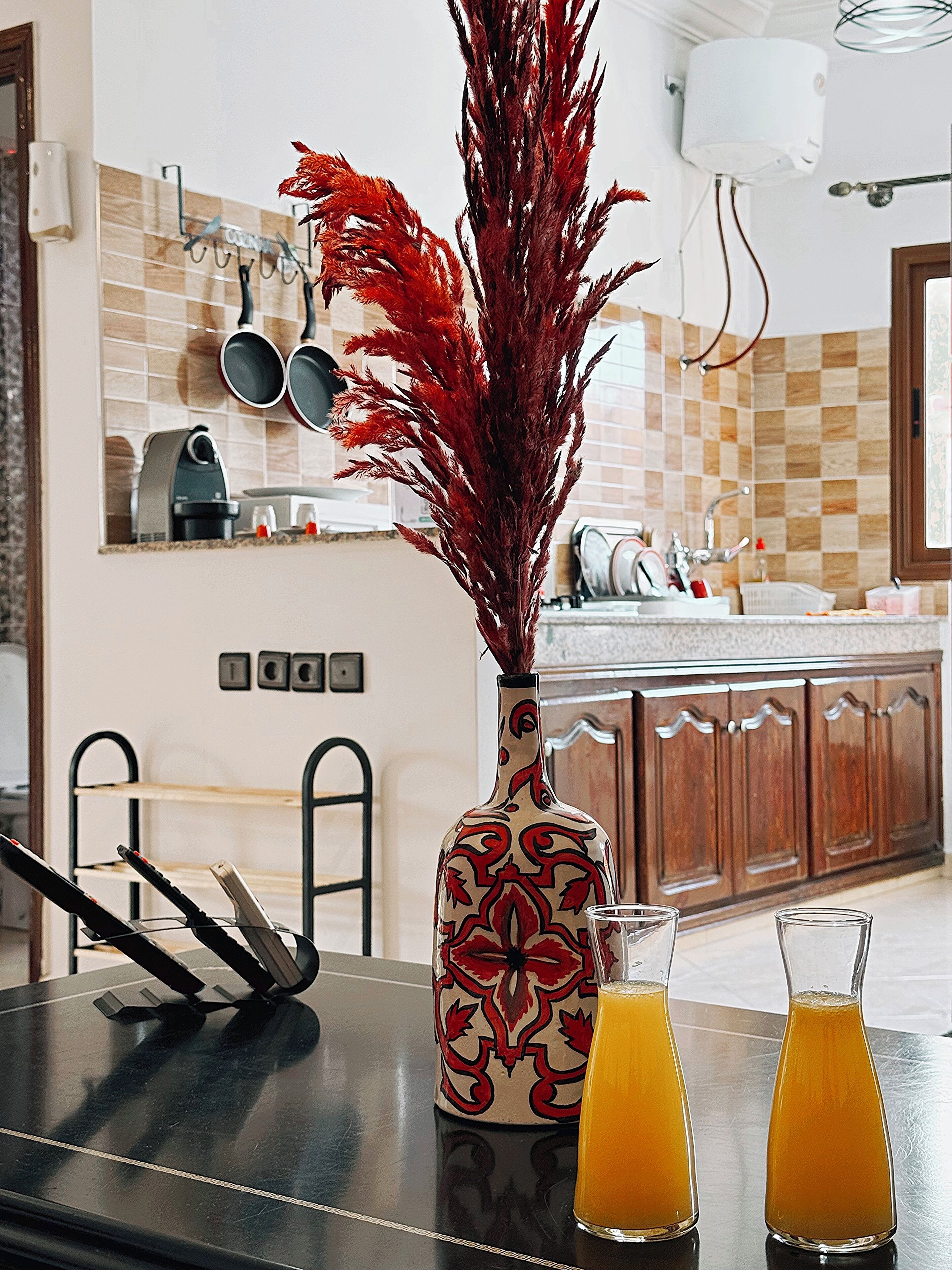 A kitchen with a vase of red foliage, two glasses of orange juice, and a coffee maker.