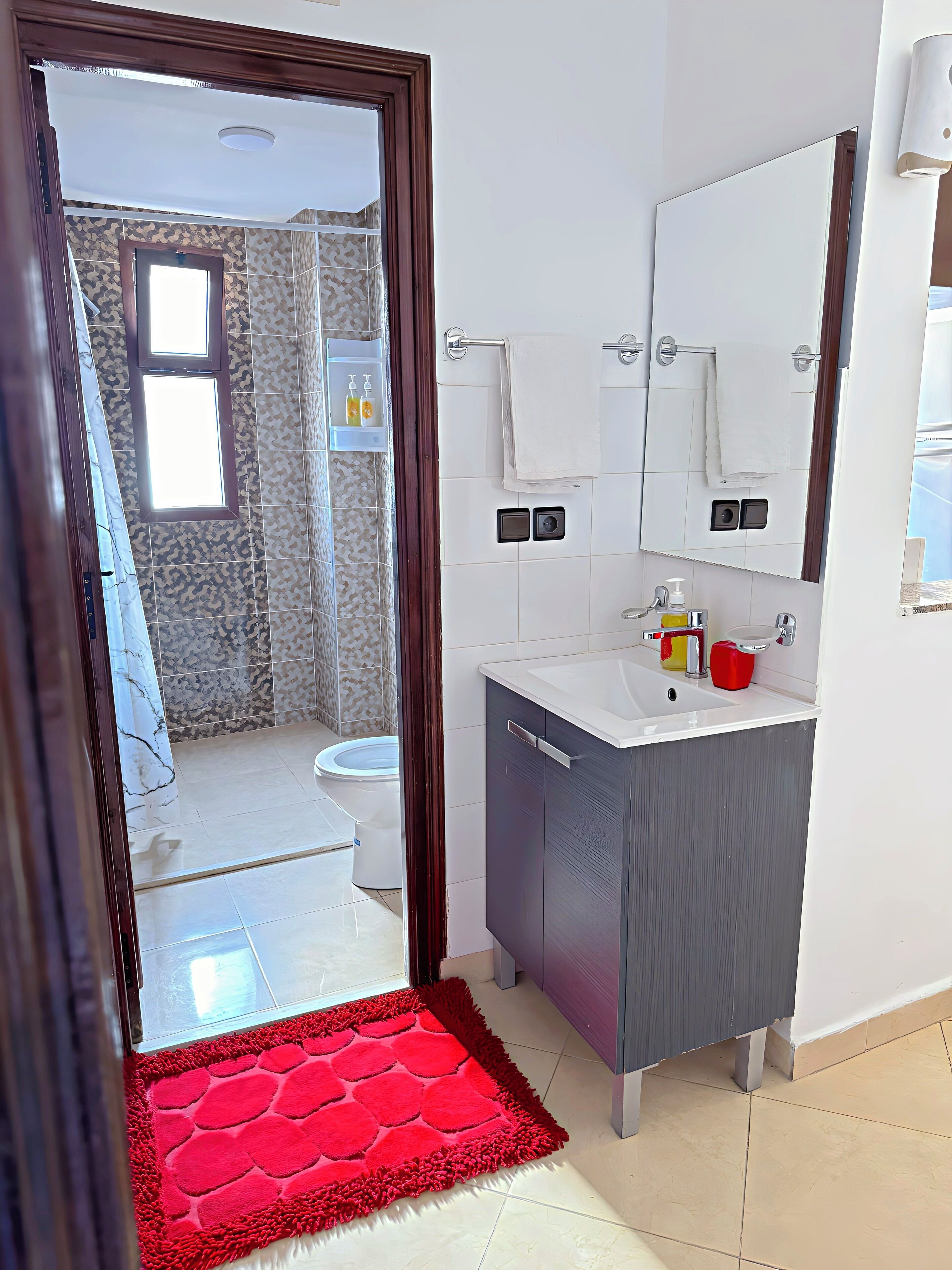 A bathroom with a toilet, sink, mirror, and a red rug leading to the door.