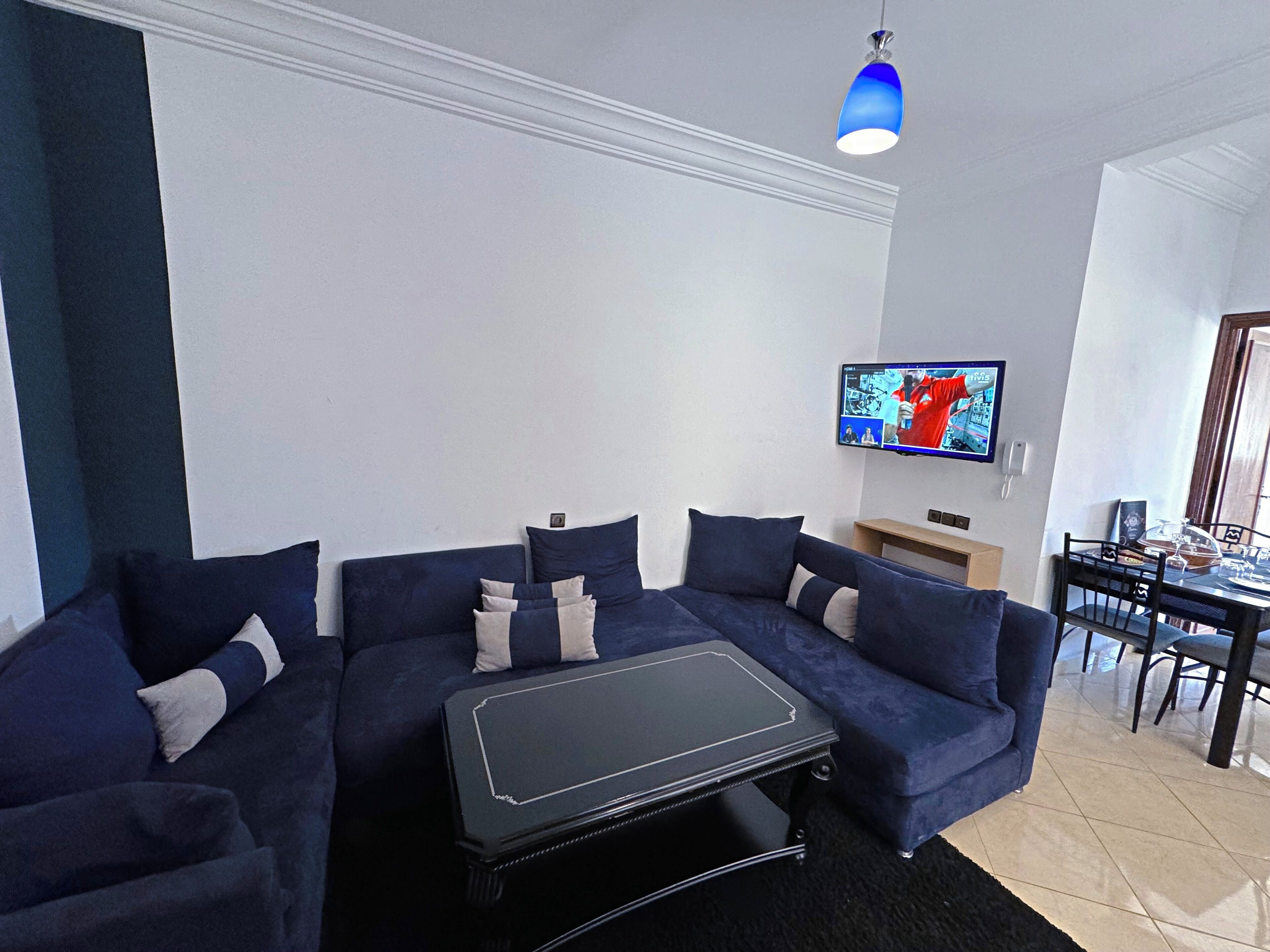 A modern living room with a sectional sofa, a black coffee table, and a flat-screen TV mounted on the wall.