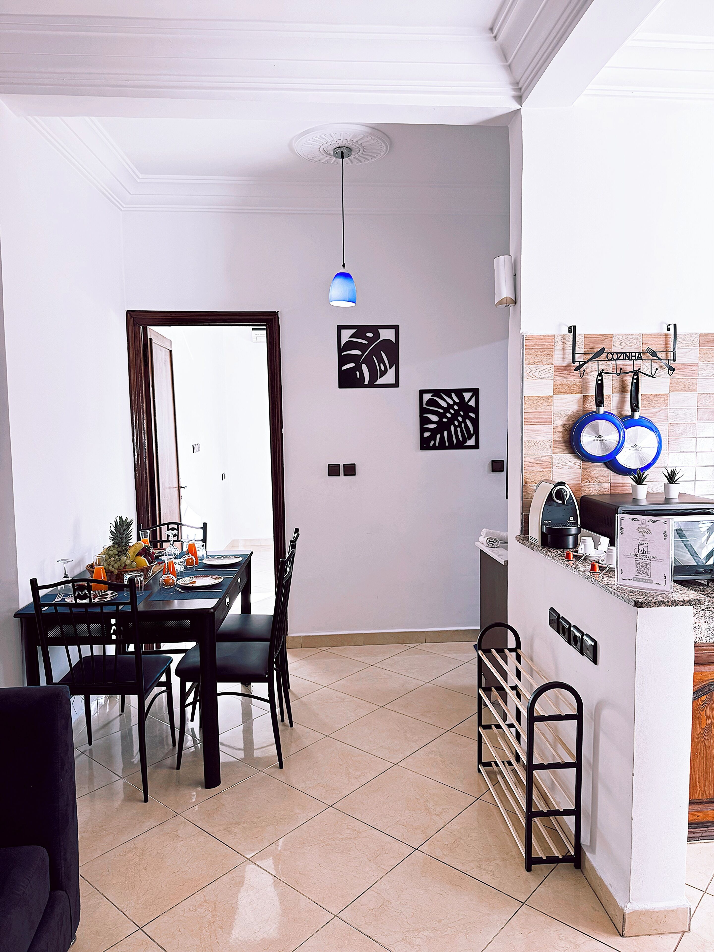 A dining area with a table set for two, a kitchen area with a coffee maker and a kettle, and a ceiling with a decorative light fixture.