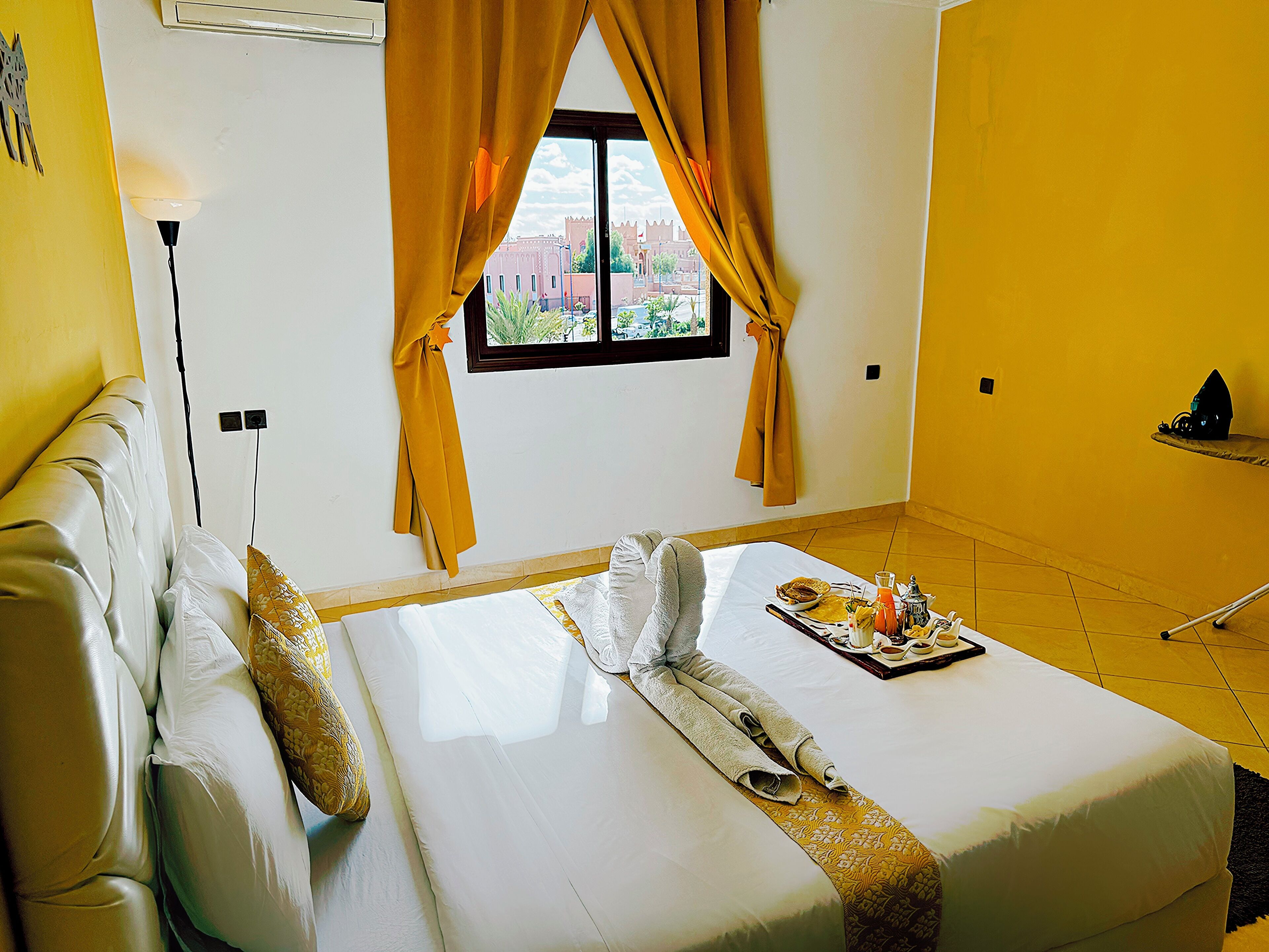 Habitación de hotel con cama, ventana con cortinas, mesita de noche y vistas a la ciudad.