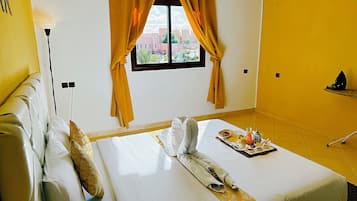 Habitación de hotel con cama, ventana con cortinas, mesita de noche y vistas a la ciudad.