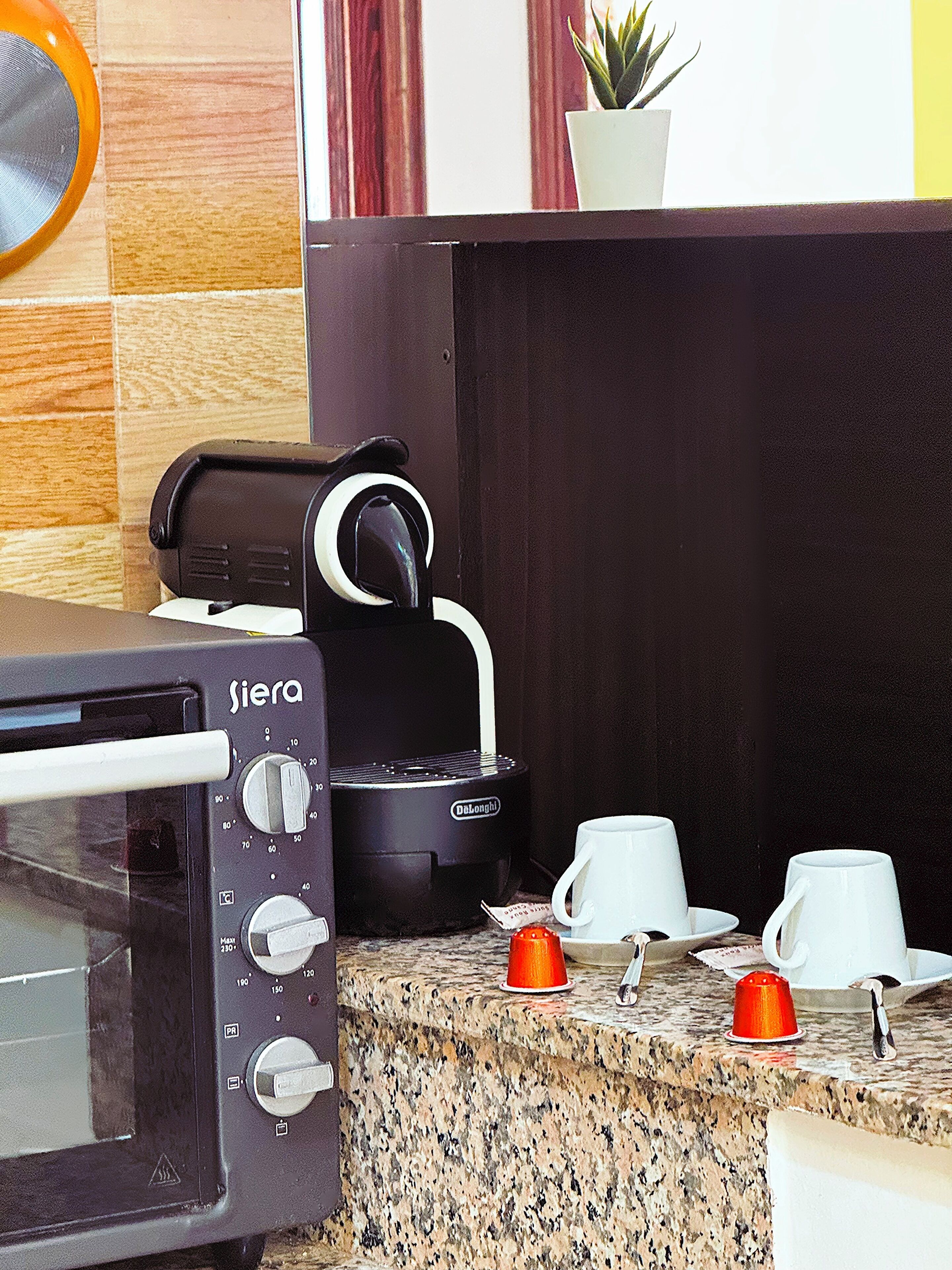 A kitchen with a toaster, a coffee maker, and a microwave. There are cups and a red cup on the counter.