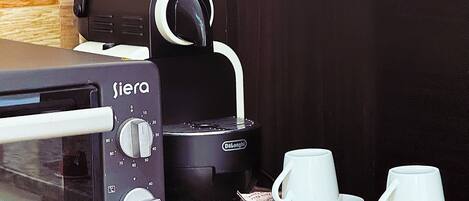A kitchen with a toaster, a coffee maker, and a microwave. There are cups and a red cup on the counter.