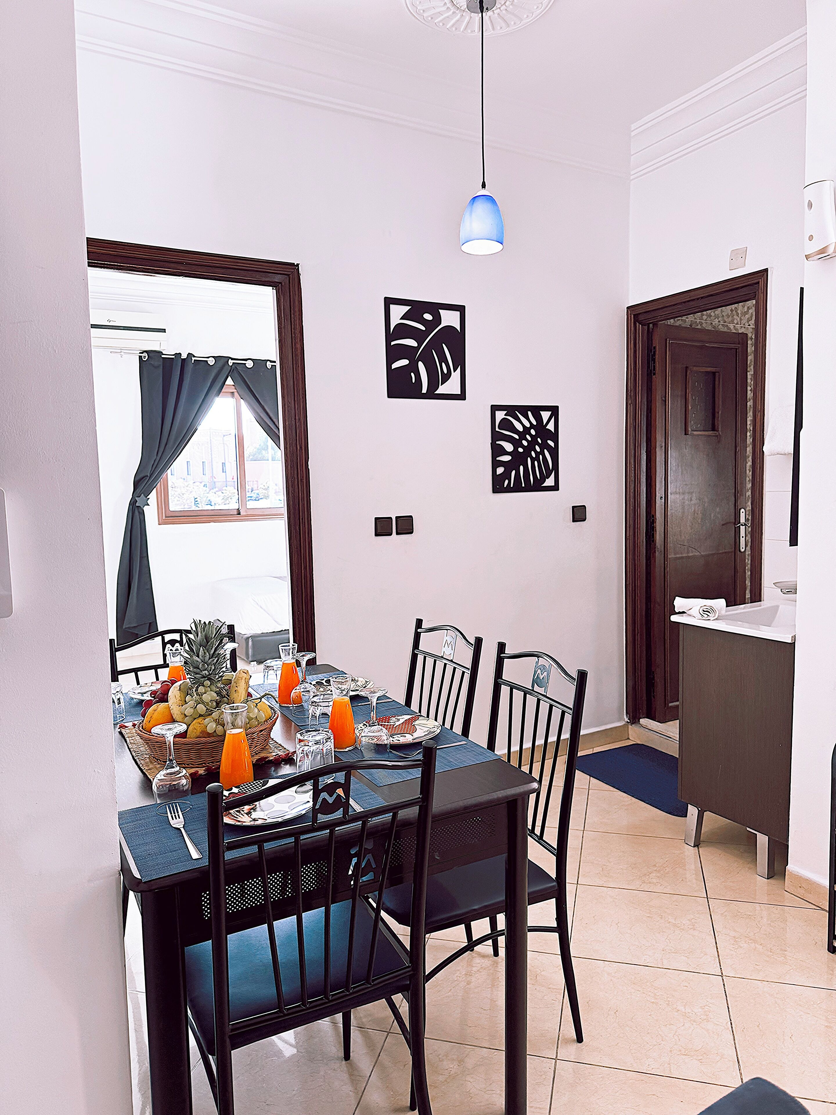 A dining area with a table set for four, chairs, a blue pendant light, and wall art.