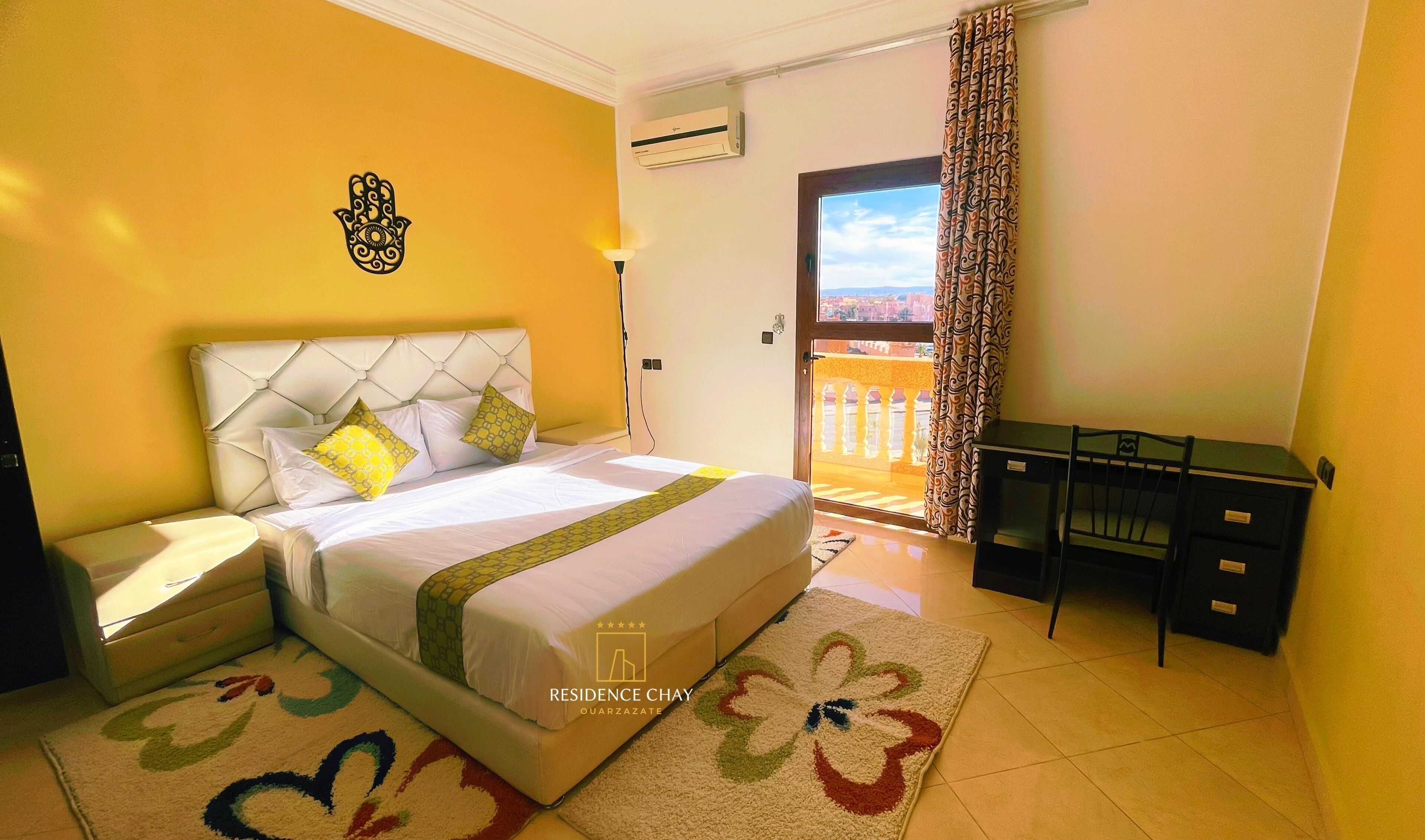 A hotel room with a bed, a desk, and a view of the outside.