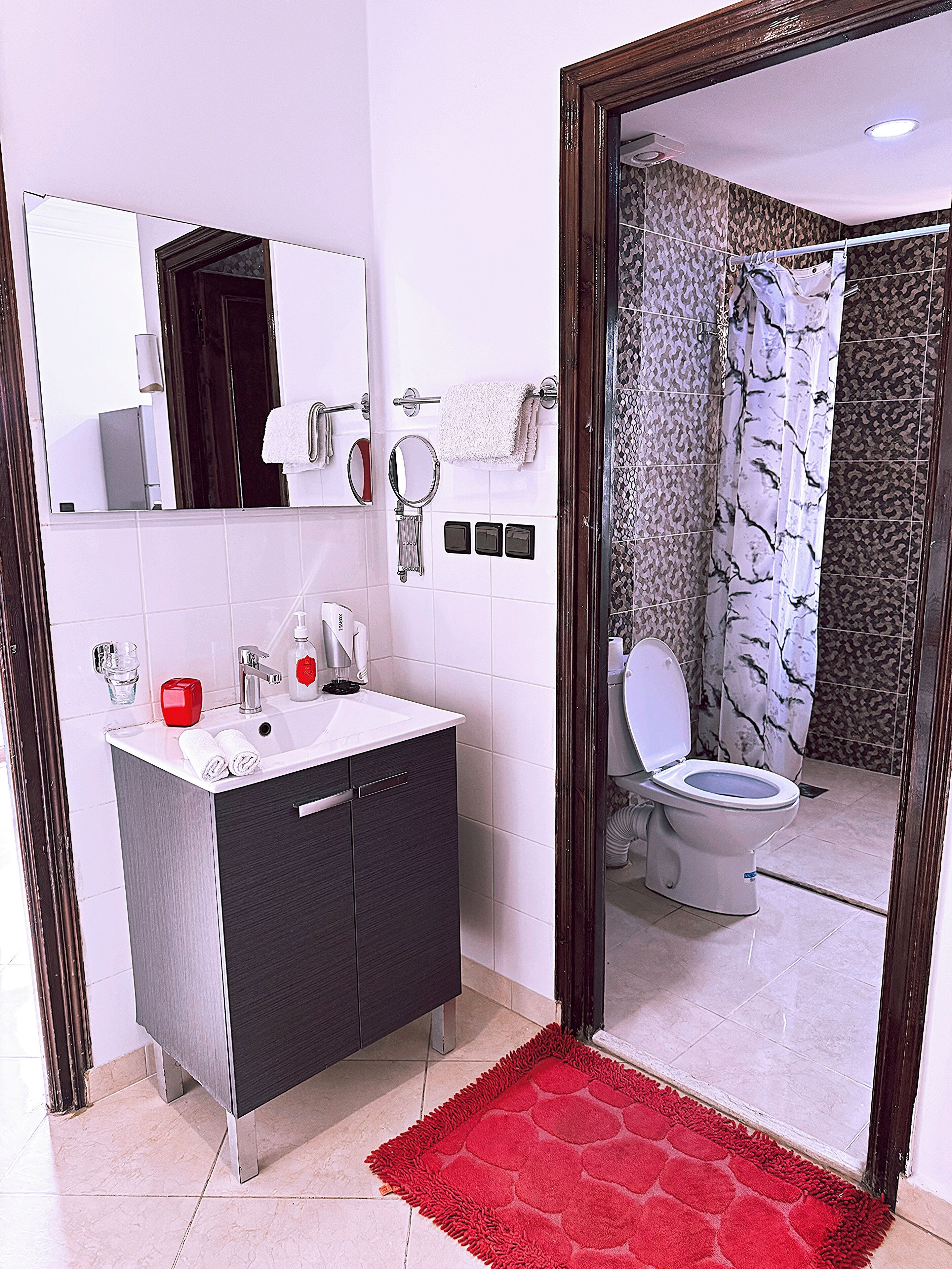 A modern bathroom with a white sink, dark vanity, and a red rug.