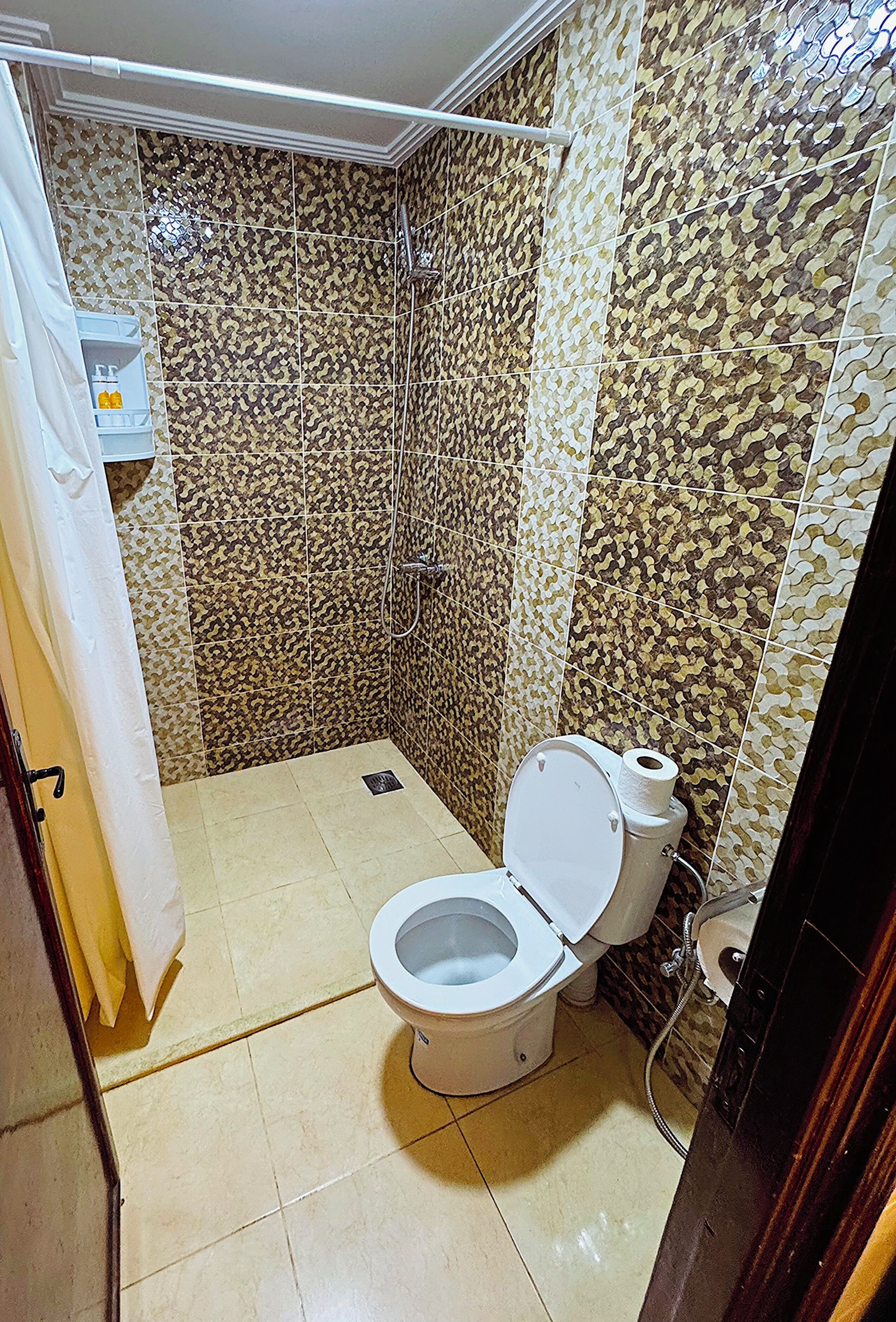 Un baño con azulejos estampados, un inodoro, una ducha y un perchero para toallas.