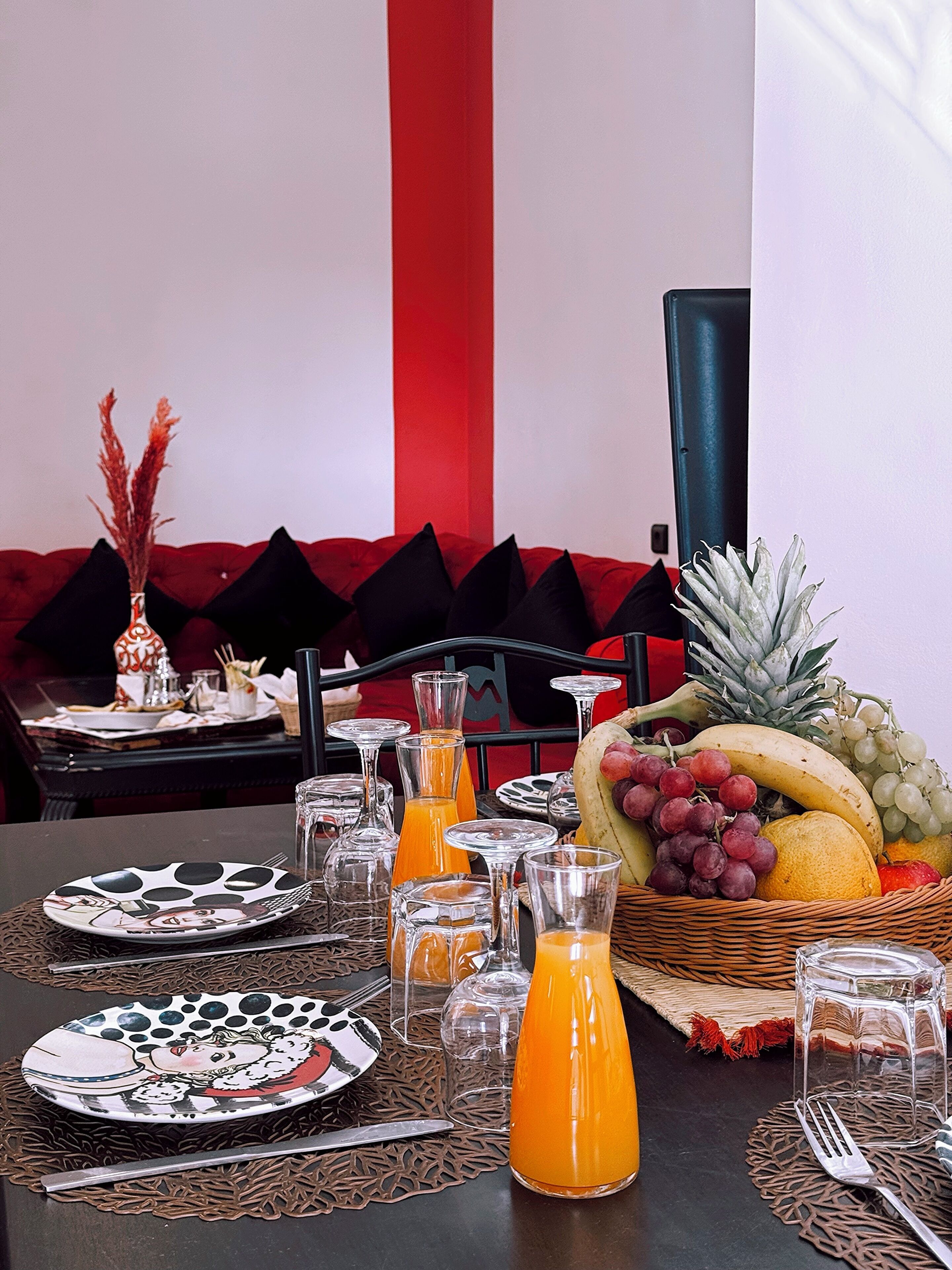 Een ontbijttafel met een fruitmand, sinaasappelsap en borden.