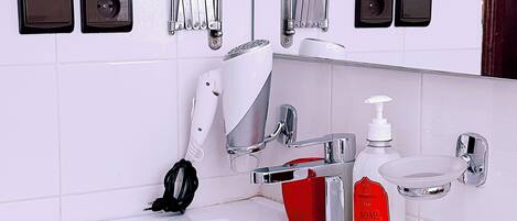 A modern bathroom with a white sink, chrome fixtures, a red soap dispenser, and two mirrors.