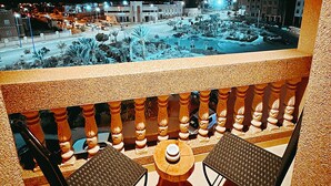 Varanda com duas cadeiras e uma mesa, com vista para a paisagem urbana à noite.