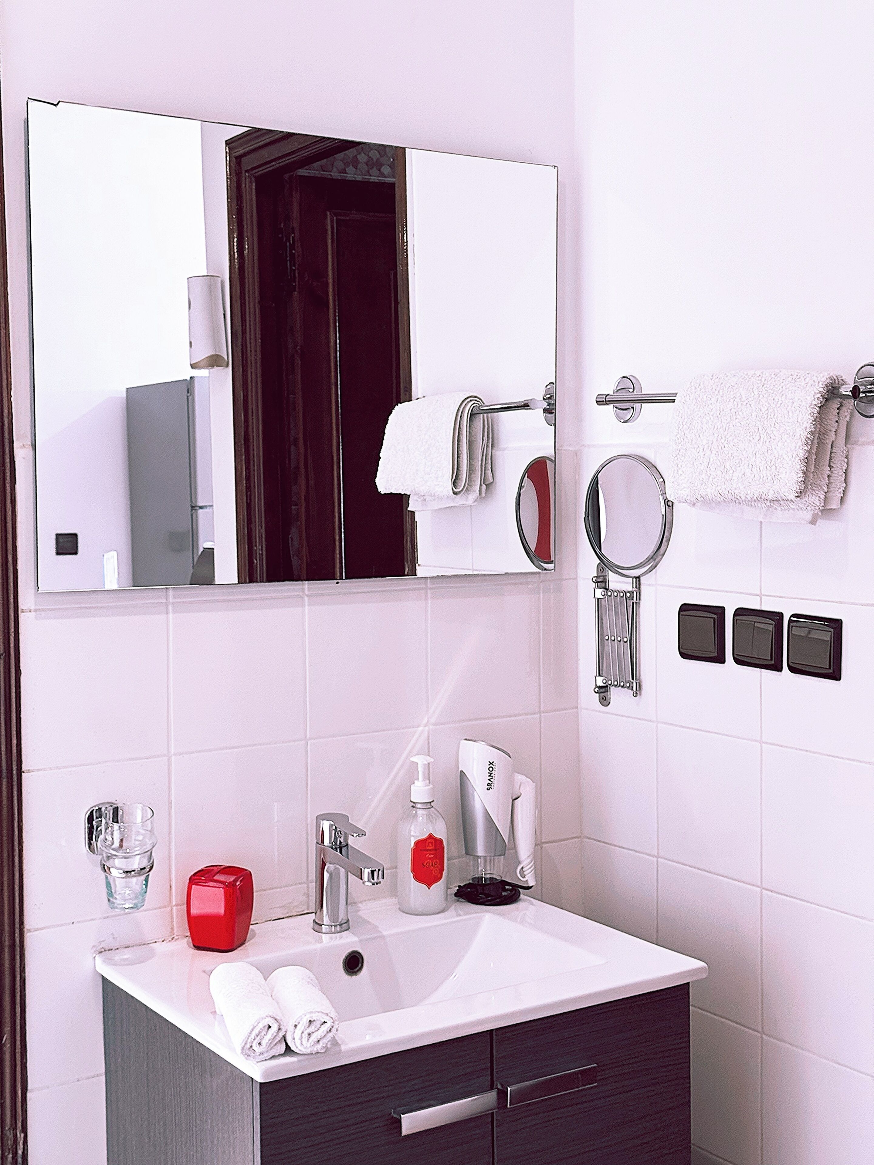 A bathroom with a white sink, a red soap dispenser, a mirror, and a towel rack.