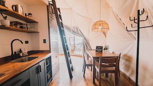 A tented kitchen with wooden shelves, a sink, and a dining table with chairs. - Ananta Dome (Monteverde)
