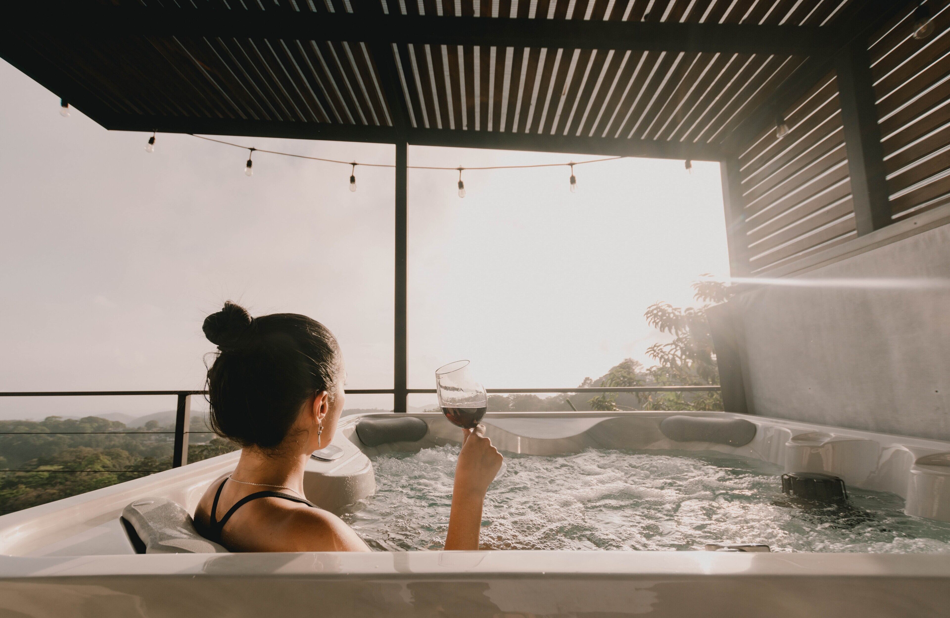 Una persona en un jacuzzi, con una copa de vino, disfrutando de un paisaje pintoresco.