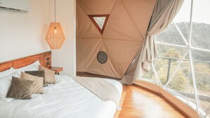 A bedroom with a large bed, wooden headboard, and a view of the outdoors through a large window. - Ananta Dome (Monteverde)