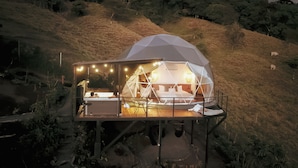 A geodesic dome structure with a balcony, interior lighting, and a bed. - Ananta Dome (Monteverde)