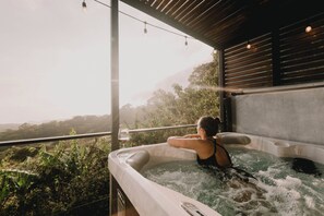 Une personne se détend dans un bain à remous, avec une vue sur un paysage luxuriant.