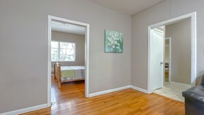 Een kamer met houten vloeren, een bed met een groene dekbedovertrek, een raam met jaloezieën en een schilderij aan de muur.