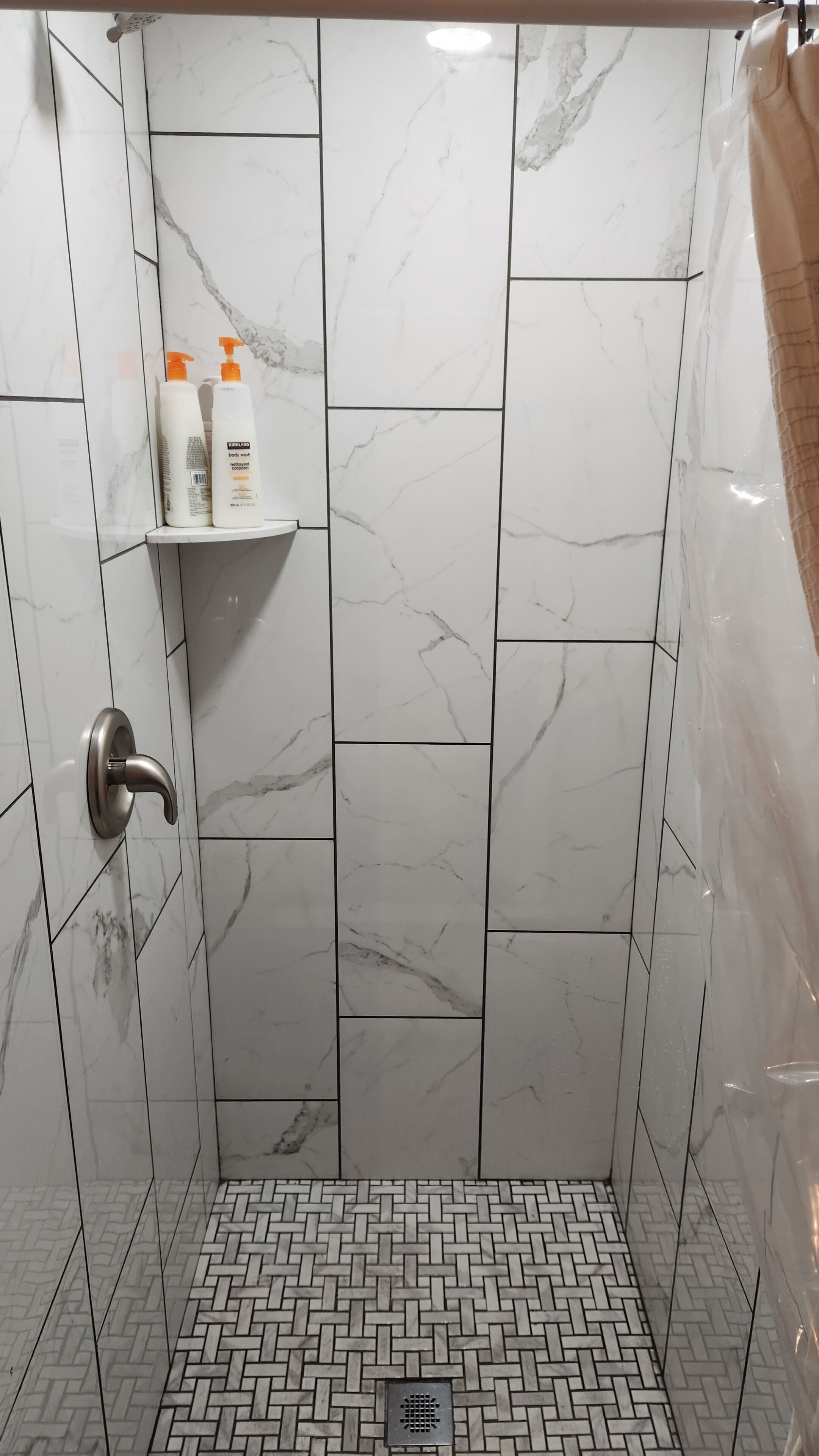 A shower with white marble tiles and a herringbone-patterned floor.