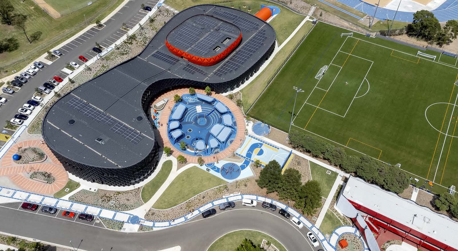 Vista aérea de un estadio con una zona central circular, estacionamientos y un campo deportivo.