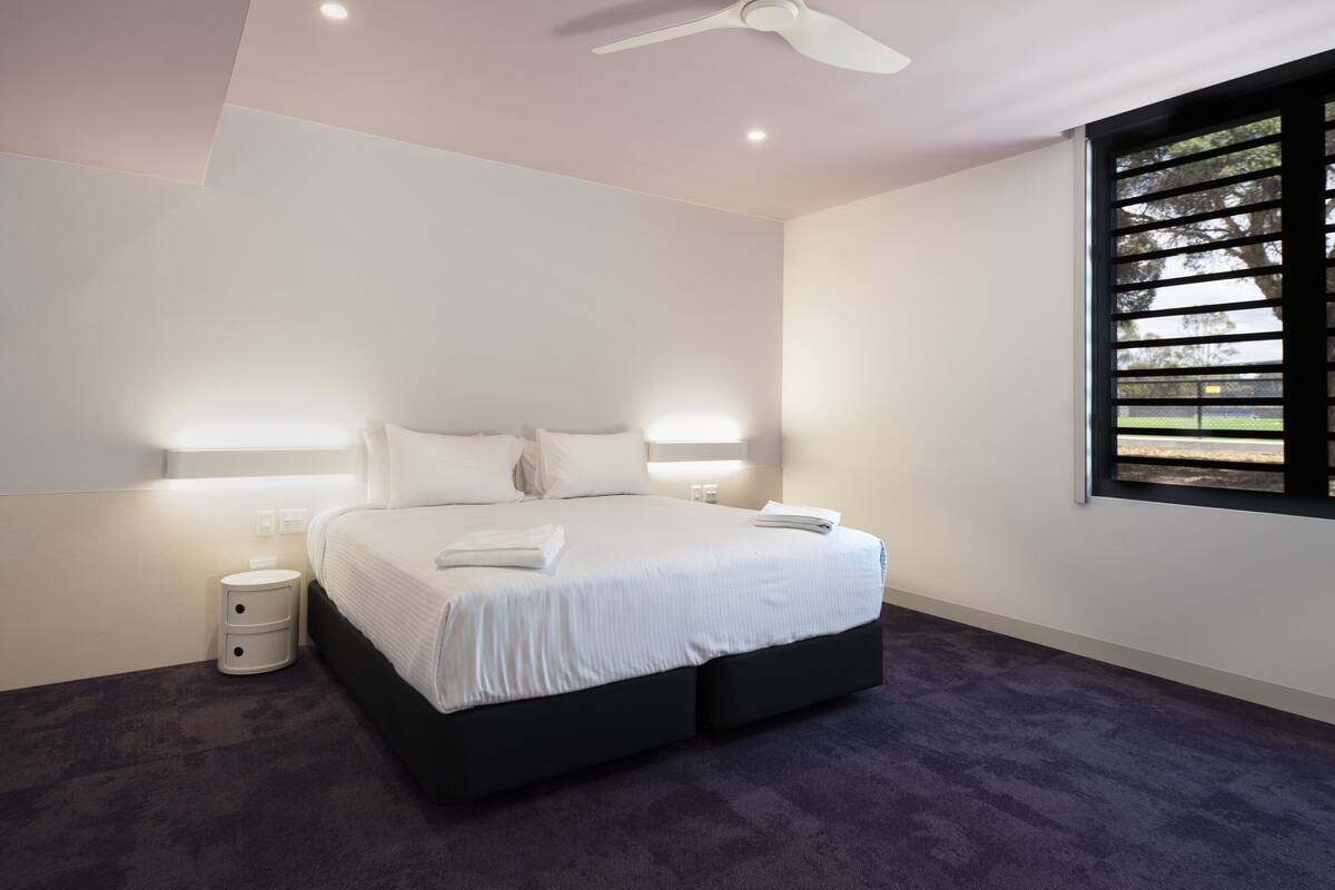 Une chambre à coucher avec un lit, des lampes de chevet, une table de chevet et une fenêtre avec des stores.
