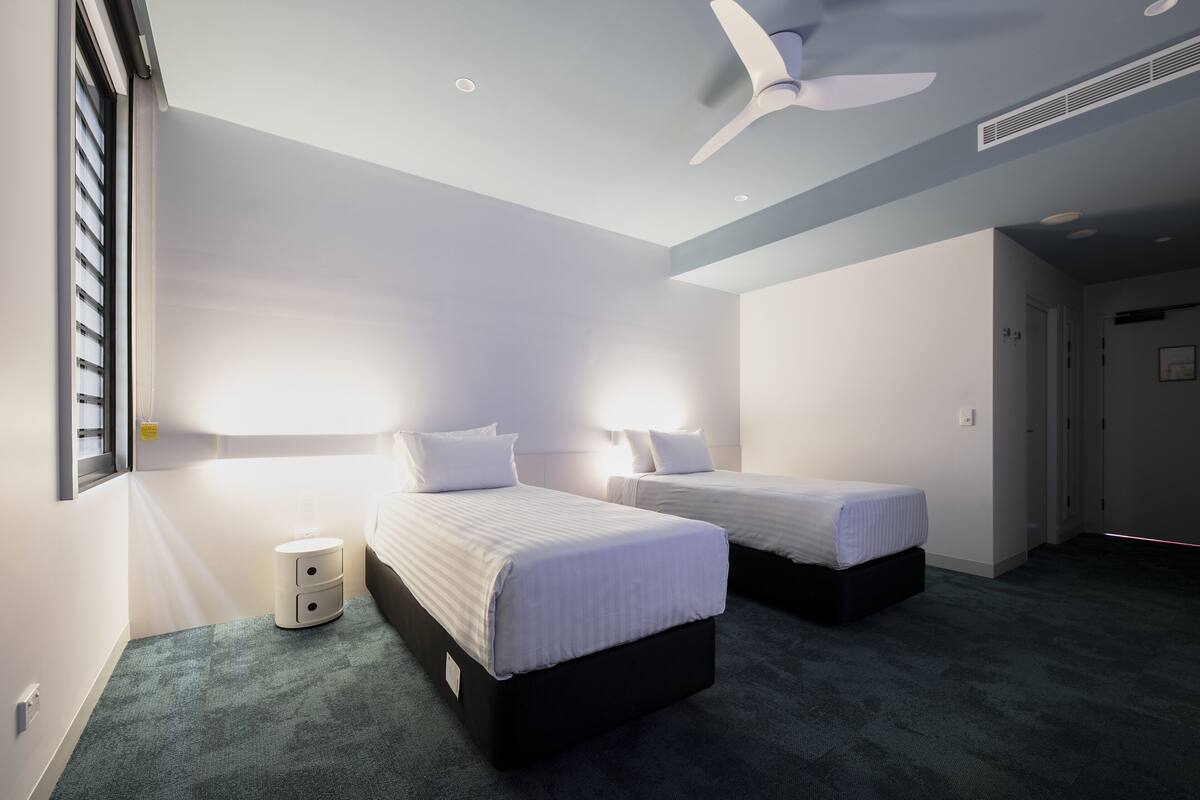 Une chambre d’hôtel avec deux lits, un ventilateur de plafond et une petite table de chevet.