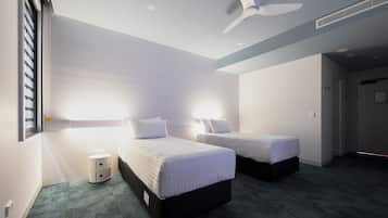 Una habitación de hotel con dos camas, un ventilador de techo y una mesita de noche pequeña.
