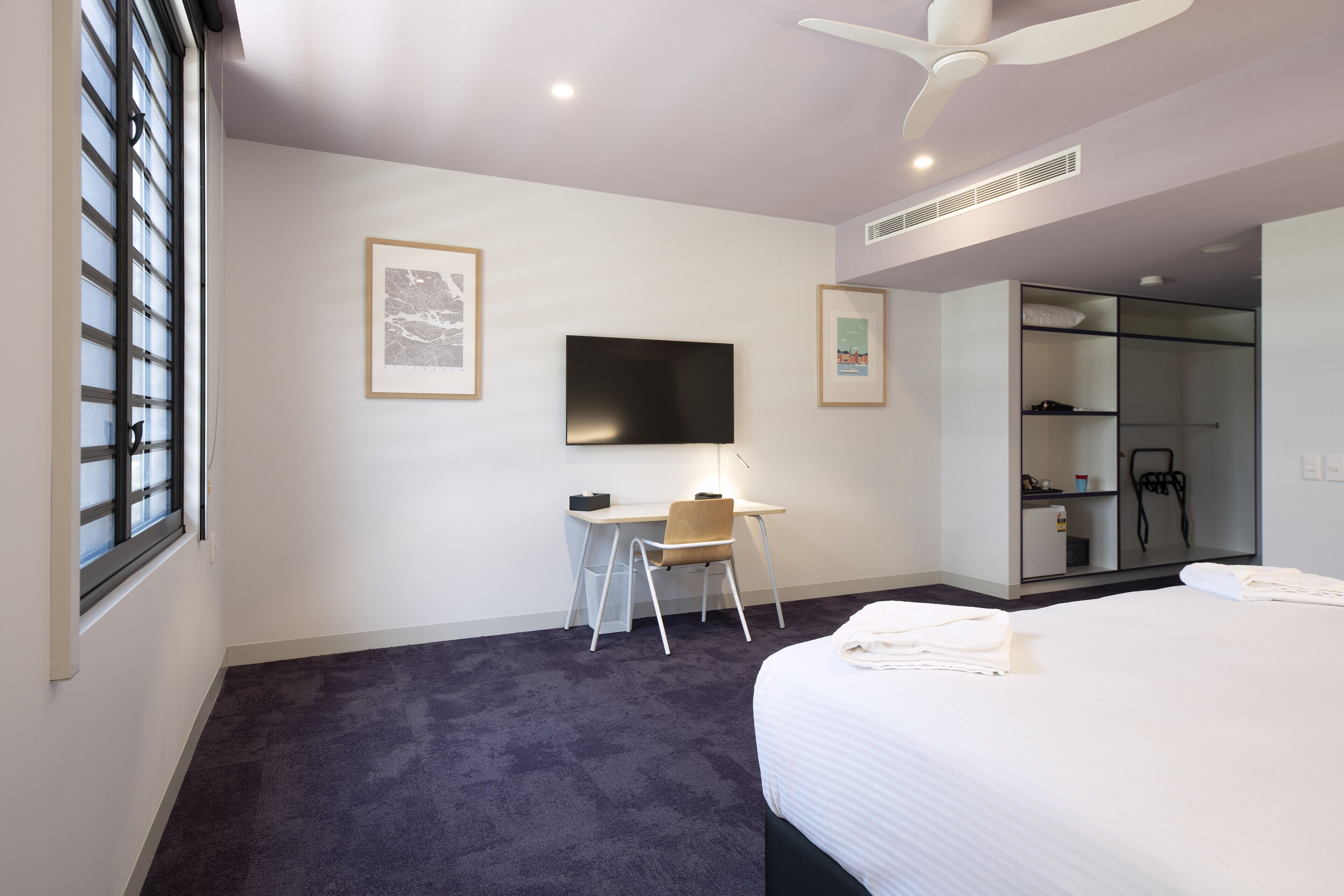 A hotel room with a bed, a desk, a chair, a television, and a wardrobe.