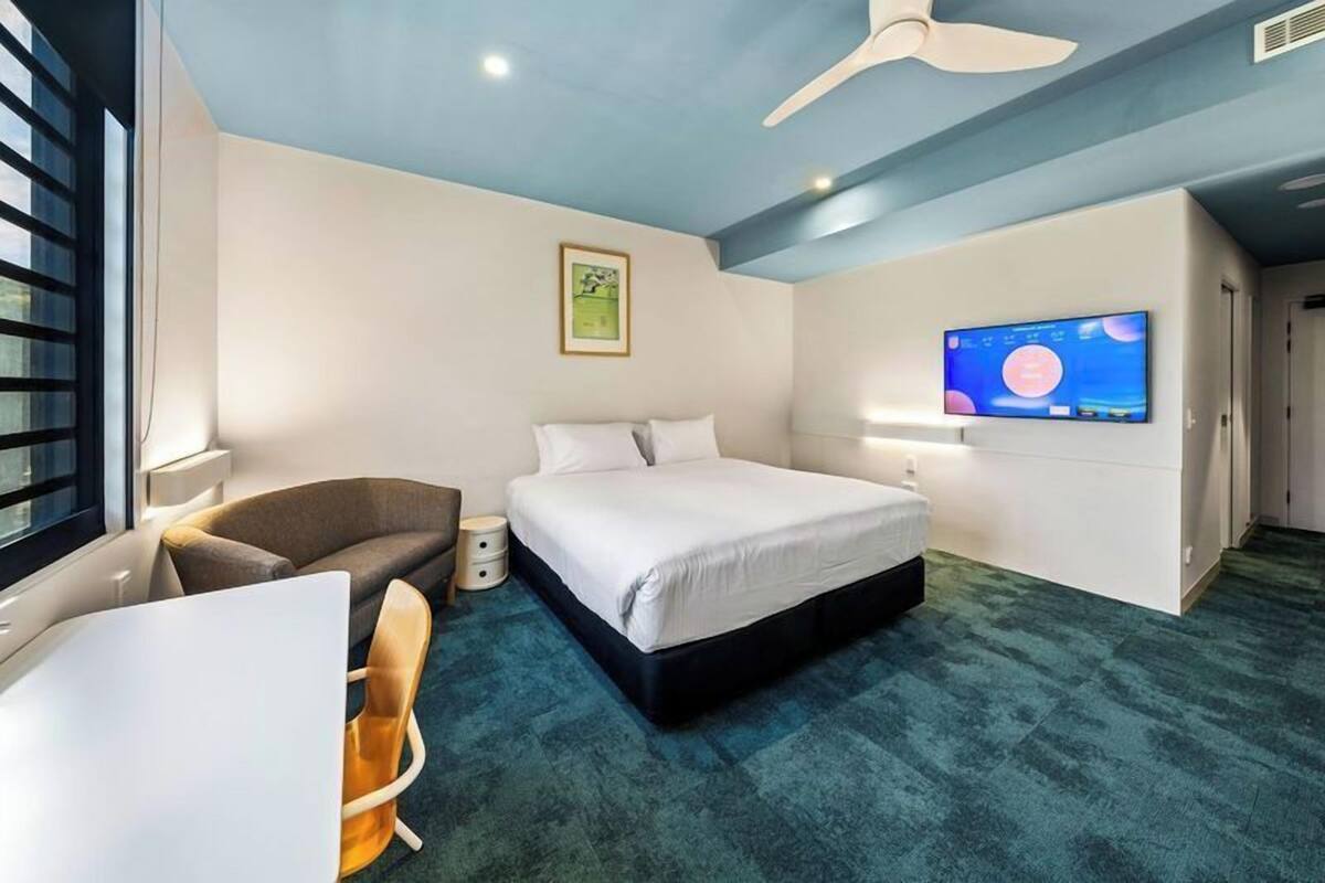 Une chambre d’hôtel moderne équipée d’un lit, d’un bureau, d’une chaise, d’une télévision et d’un ventilateur de plafond.
