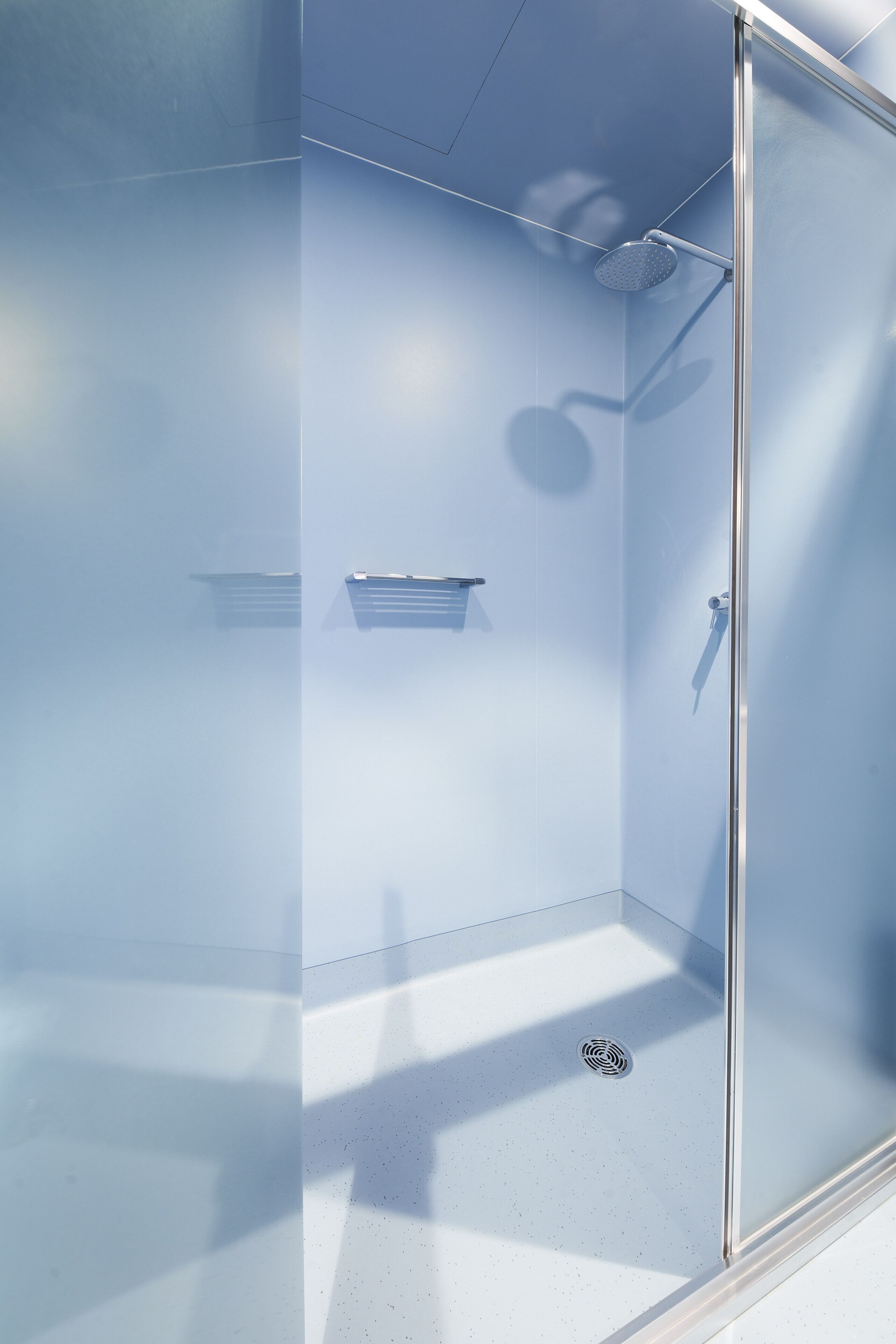 A modern shower with a glass door, a handheld showerhead, and a small shelf.
