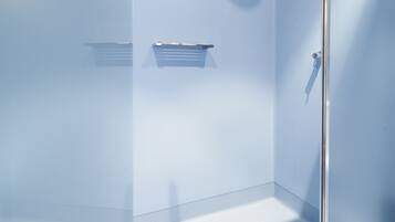 A modern shower with a glass door, a handheld showerhead, and a small shelf.