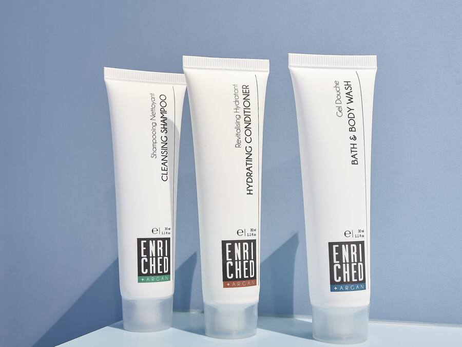 Three white tubes of Enriched Argan hair care products on a light blue surface against a light blue background.
