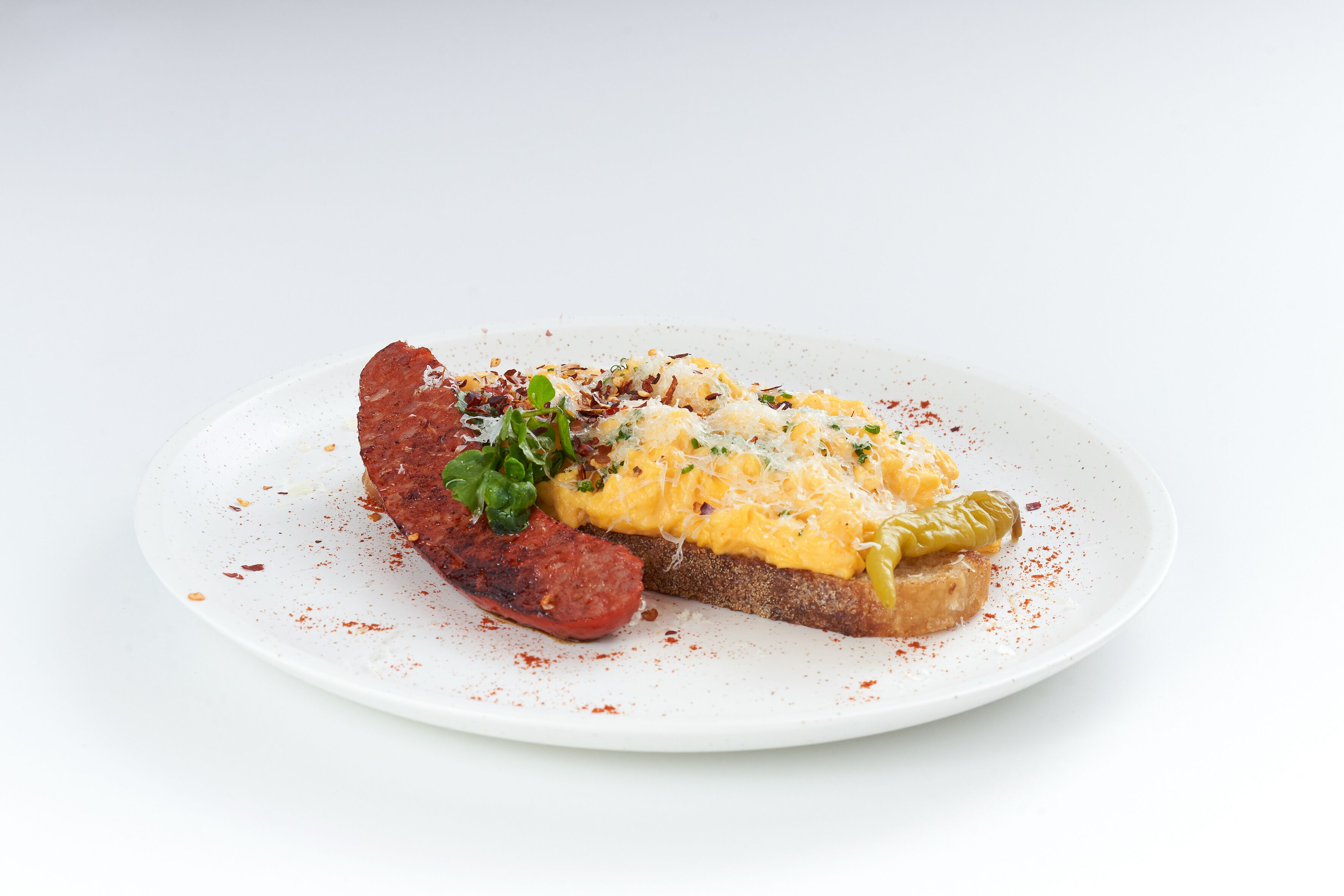 A plate with a slice of bread topped with cheese, a red sauce, and a green garnish.