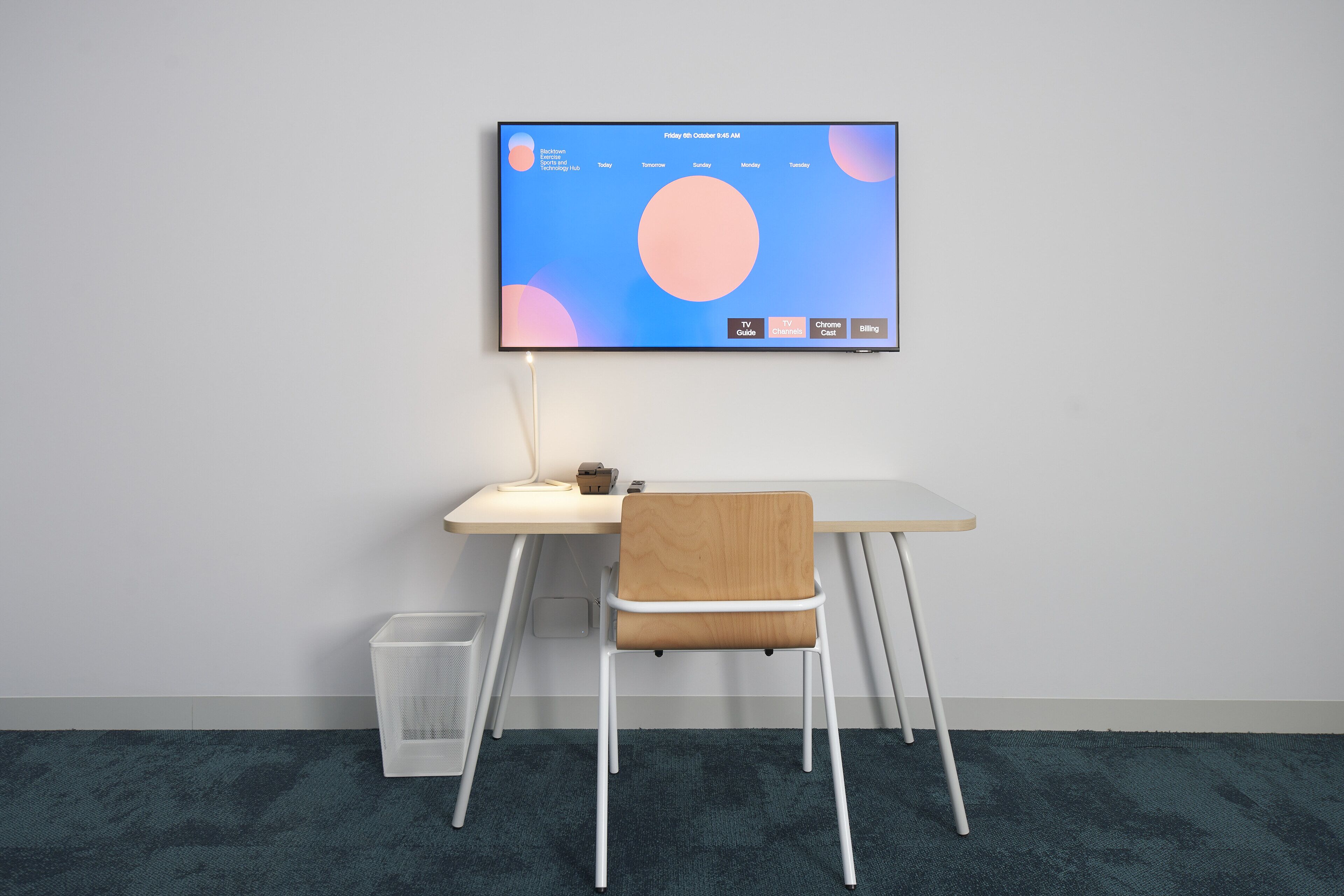 A modern workspace with a desk, chair, and a mounted computer monitor displaying a calendar.