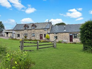 A stone building with multiple windows and doors, a grassy lawn, and a wooden fence. - Smiddy Cottage, Hawkridge (Nr Dulverton)