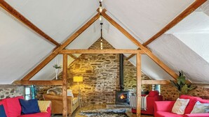 Acogedor dormitorio en un ático con pared de piedra, chimenea, vigas de madera y sofás rojos.