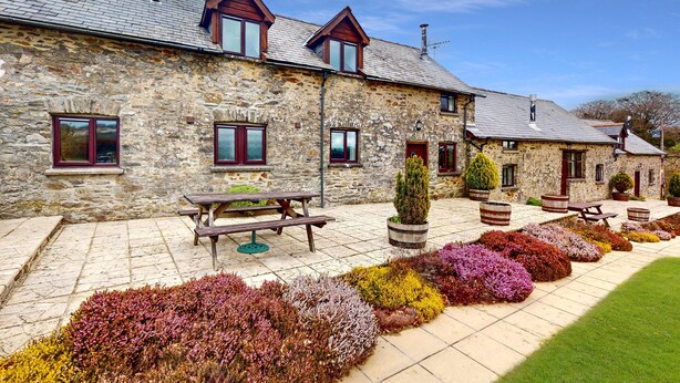 A stone building with a tiled patio, wooden benches, and a row of flower beds.