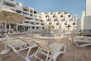 A pool area with sun loungers and umbrellas, surrounded by a multi-story building with balconies. - Penthous 2 Bed room - Jacuzzi - Terrace - Pool (Costa Adeje)