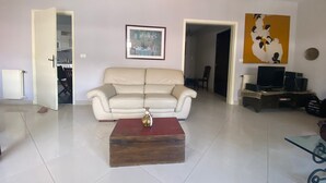 Un salon avec un canapé beige, une table basse en bois, un tableau encadré au mur et un téléviseur posé sur un meuble.